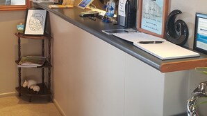 A hotel reception desk with a computer, a framed welcome sign, a small shelf with decorative items, and a wall-mounted flag. - 299 on Devon West (New Plymouth)