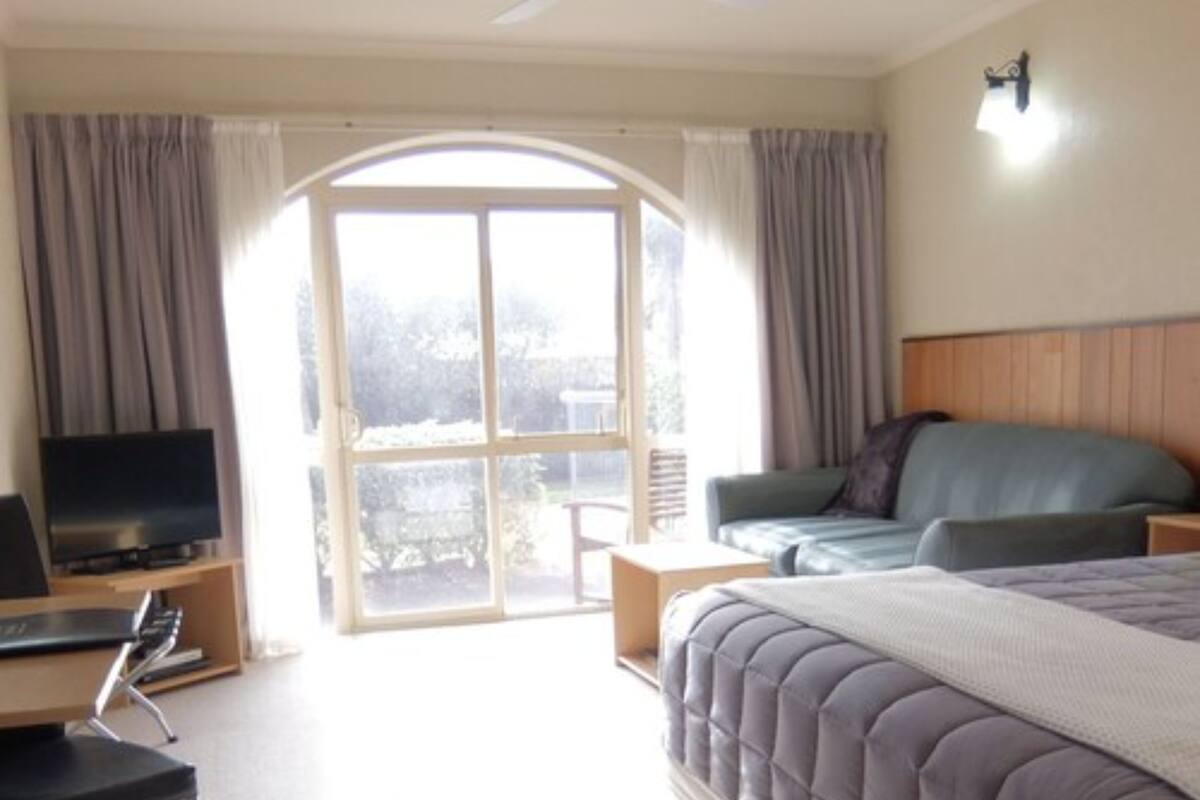 A hotel room with a bed, a desk with a computer, a television, and a view of the outdoors through a large window.
