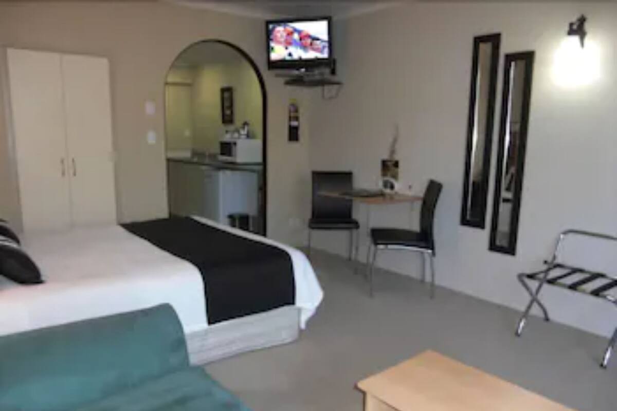 A hotel room with a bed, a desk, a chair, a TV, and a wardrobe.