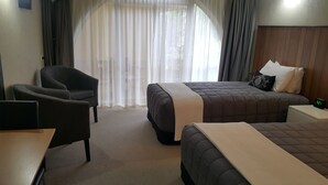 A hotel room with a bed, a chair, a small table, and a nightstand with a clock. - 299 on Devon West (New Plymouth)