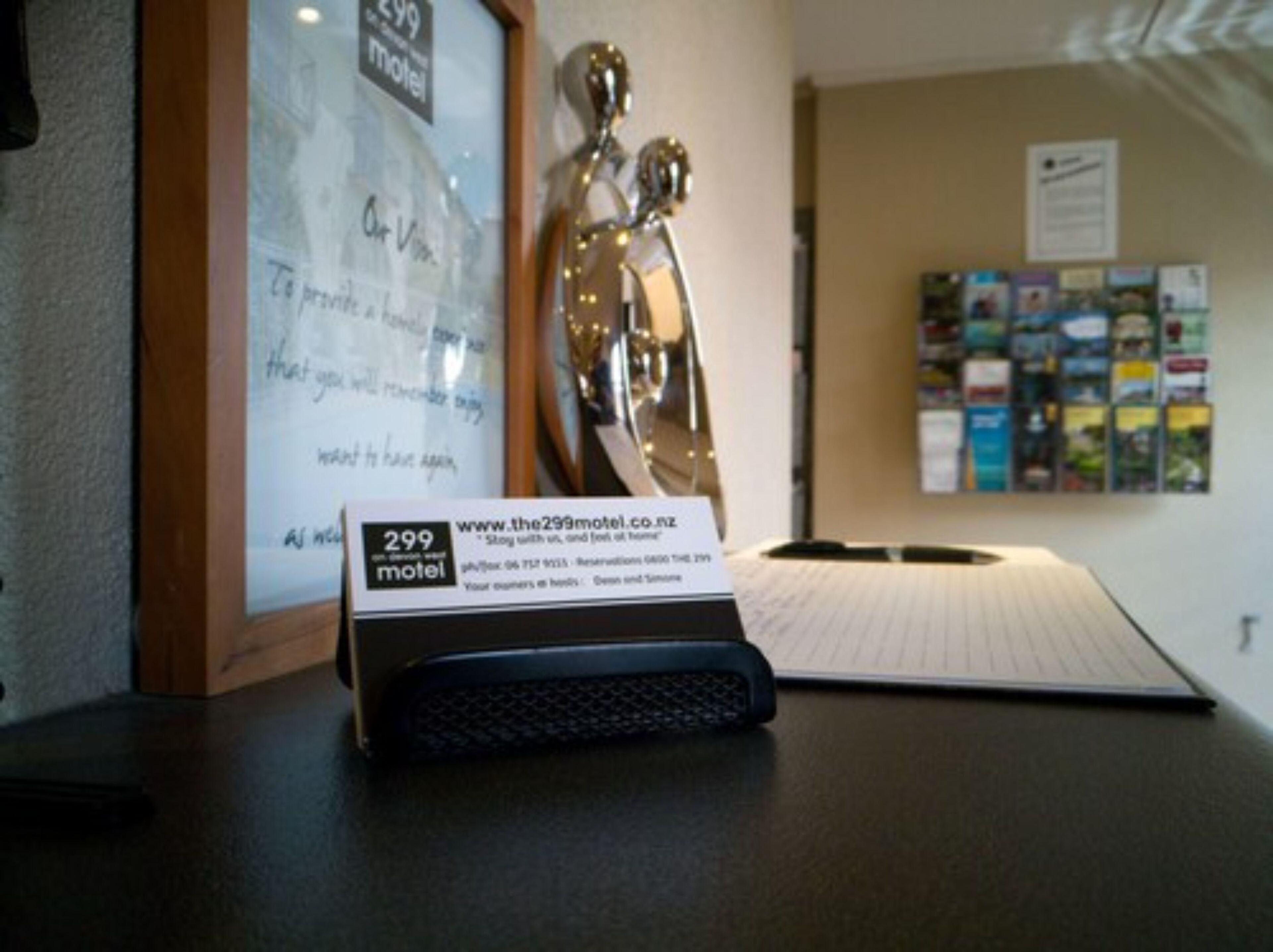 A desk with a framed sign for The 299 Motel, a black telephone, and a bulletin board with various notices.