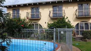 A residential building with a swimming pool, balconies, and a fenced garden area.