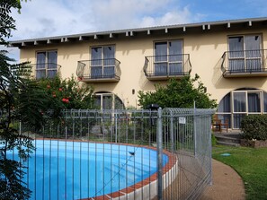 Un edificio residencial con piscina, balcones y un jardín cercado.