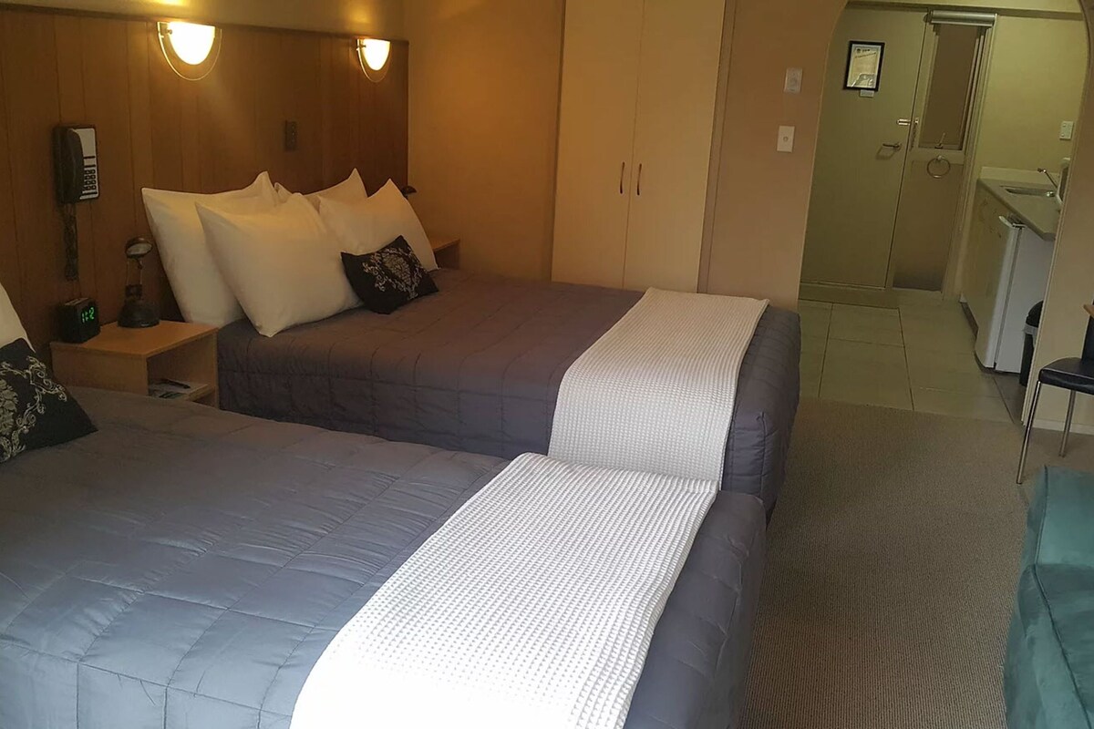A hotel room with two beds, a desk, and a kitchenette.