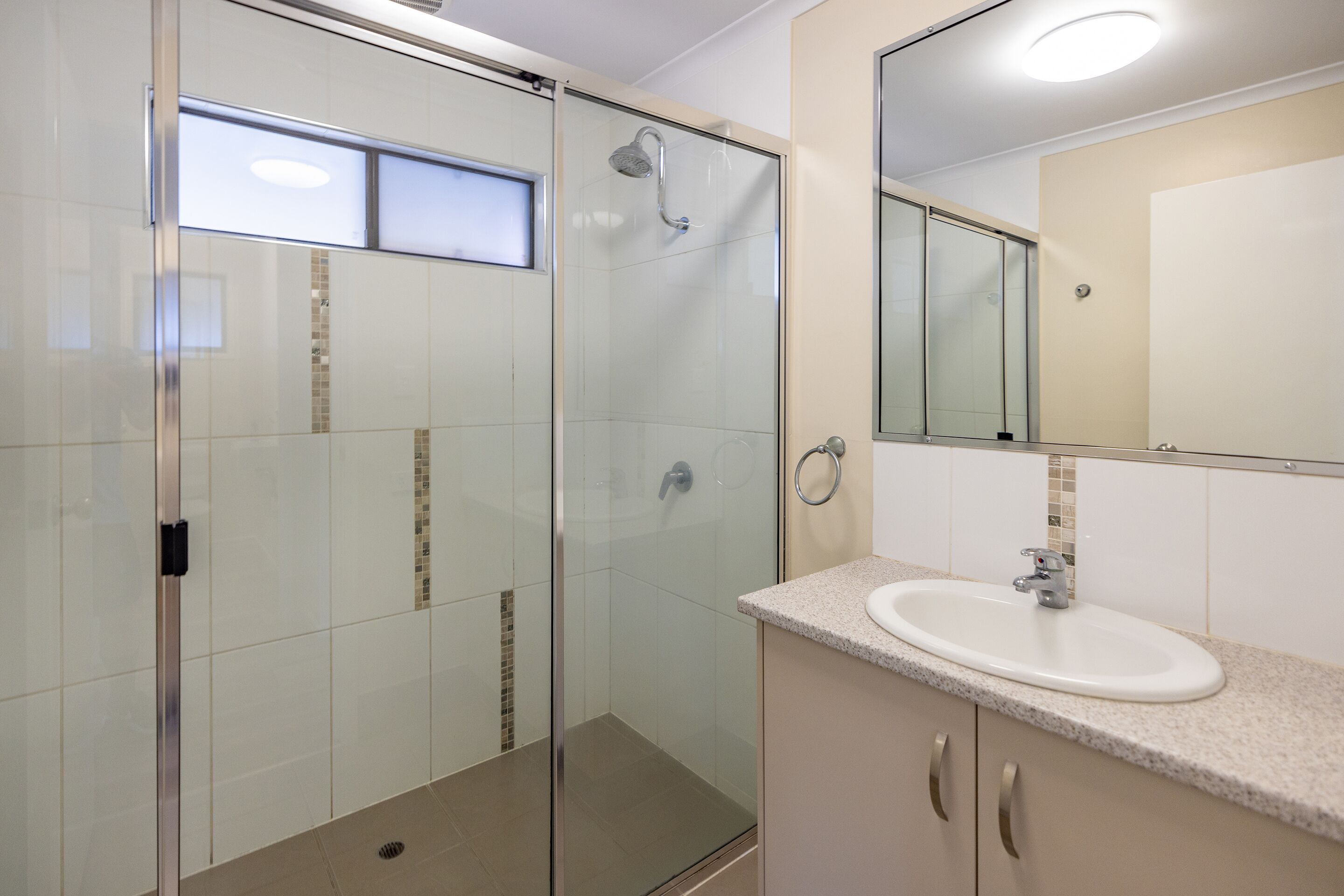 Un baño moderno con cabina de ducha de vidrio, lavamanos con espejo y suelo de baldosas.