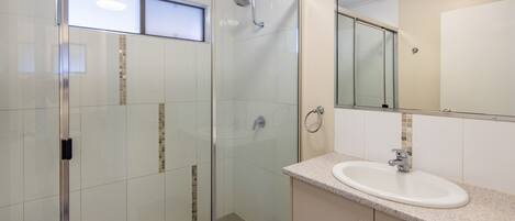 Un baño moderno con cabina de ducha de vidrio, lavamanos con espejo y suelo de baldosas.