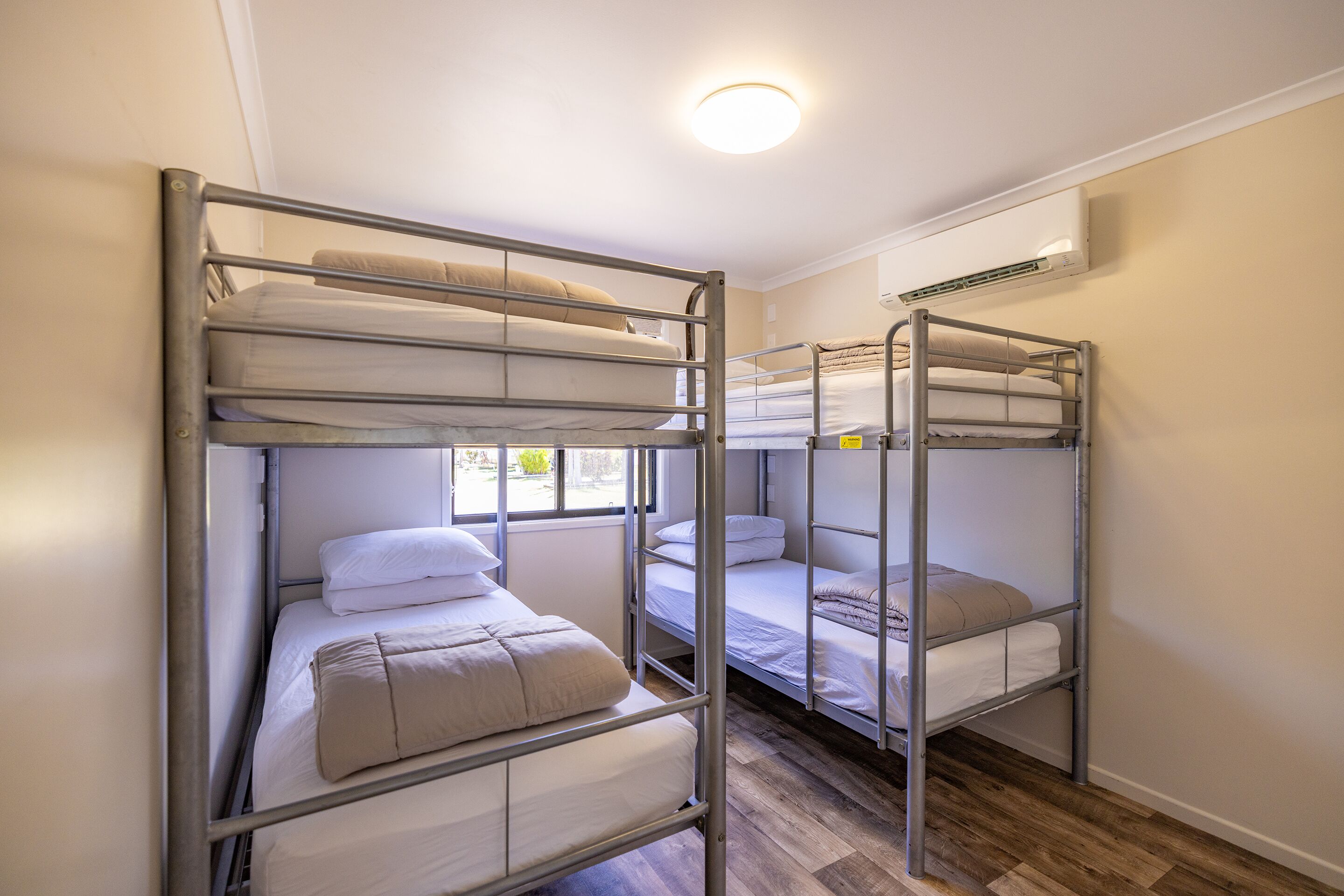 A dormitory room with bunk beds, a window, and an air conditioning unit.