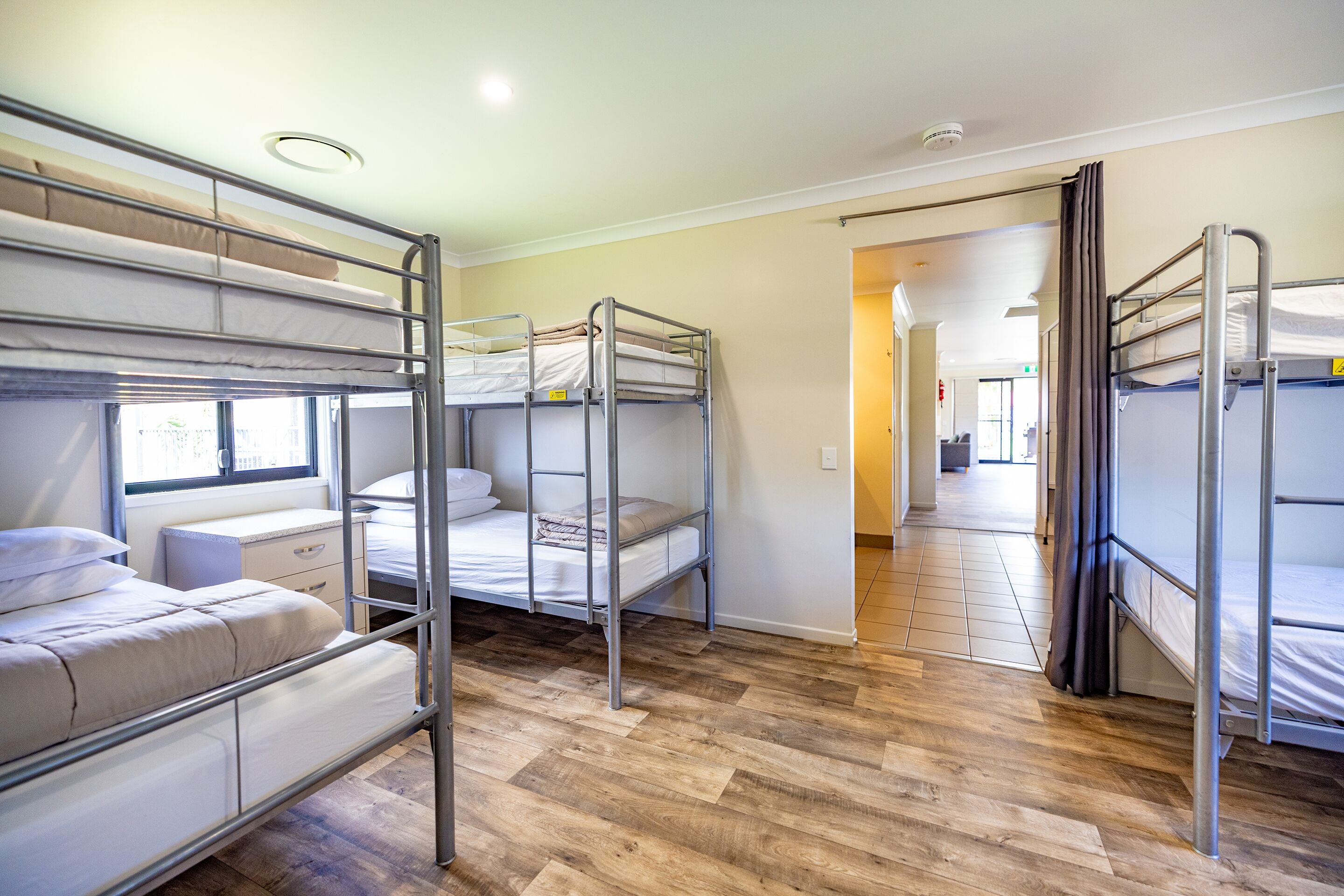 A dormitory room with bunk beds, wooden flooring, and a window providing natural light.