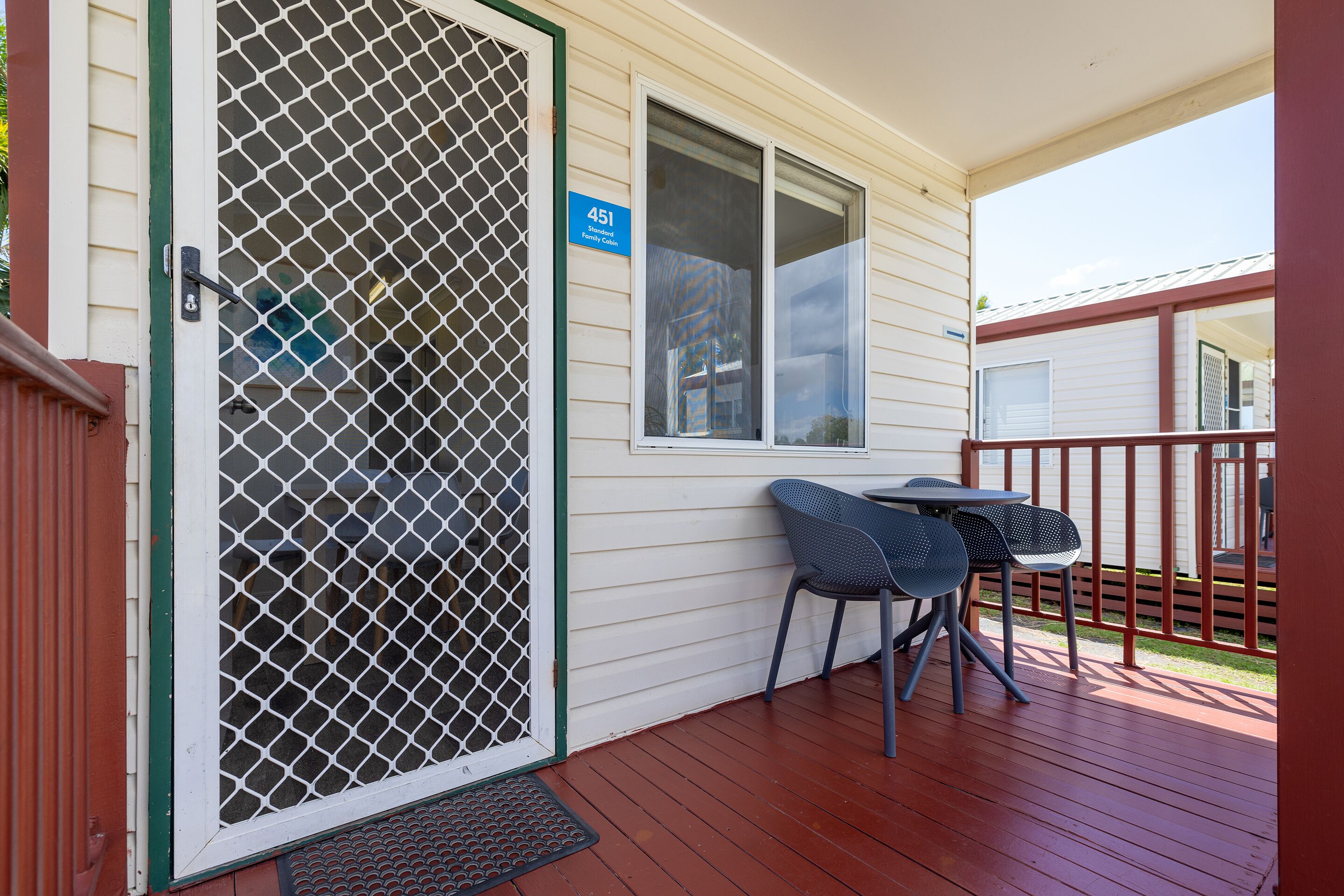 A covered porch with a wooden deck, a metal gate, and two chairs.