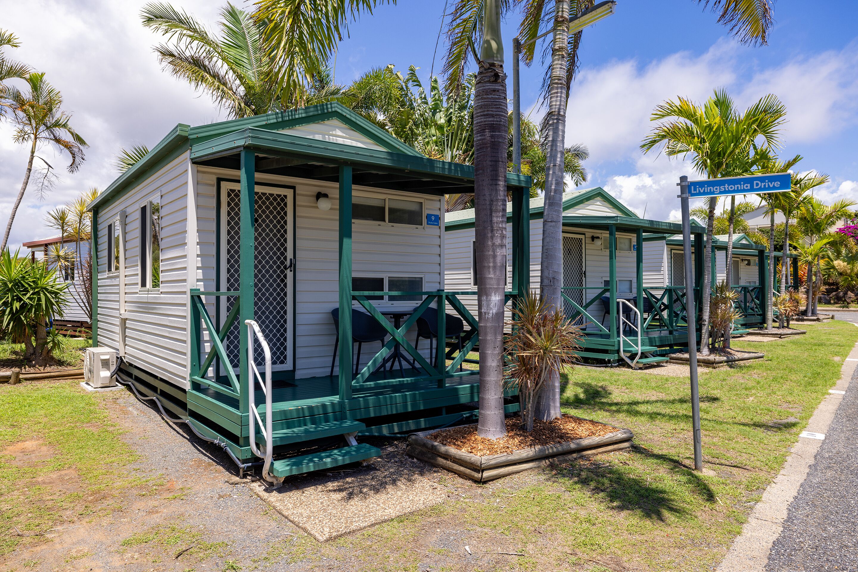 A row of small, single-story cabins with green trim and a covered porch, each with a number sign above the door.