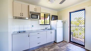 Cozinha moderna com armários brancos, micro-ondas, geladeira e janela com vista para vegetação.