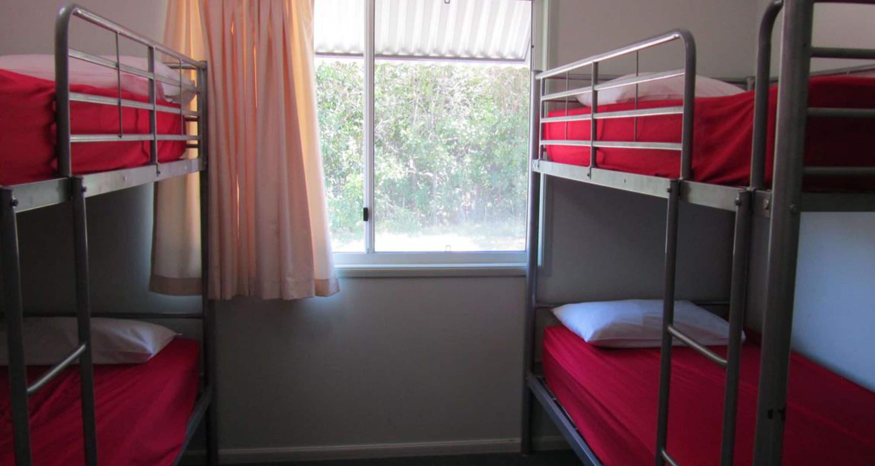 A room with bunk beds, a window with curtains, and a view of greenery outside.