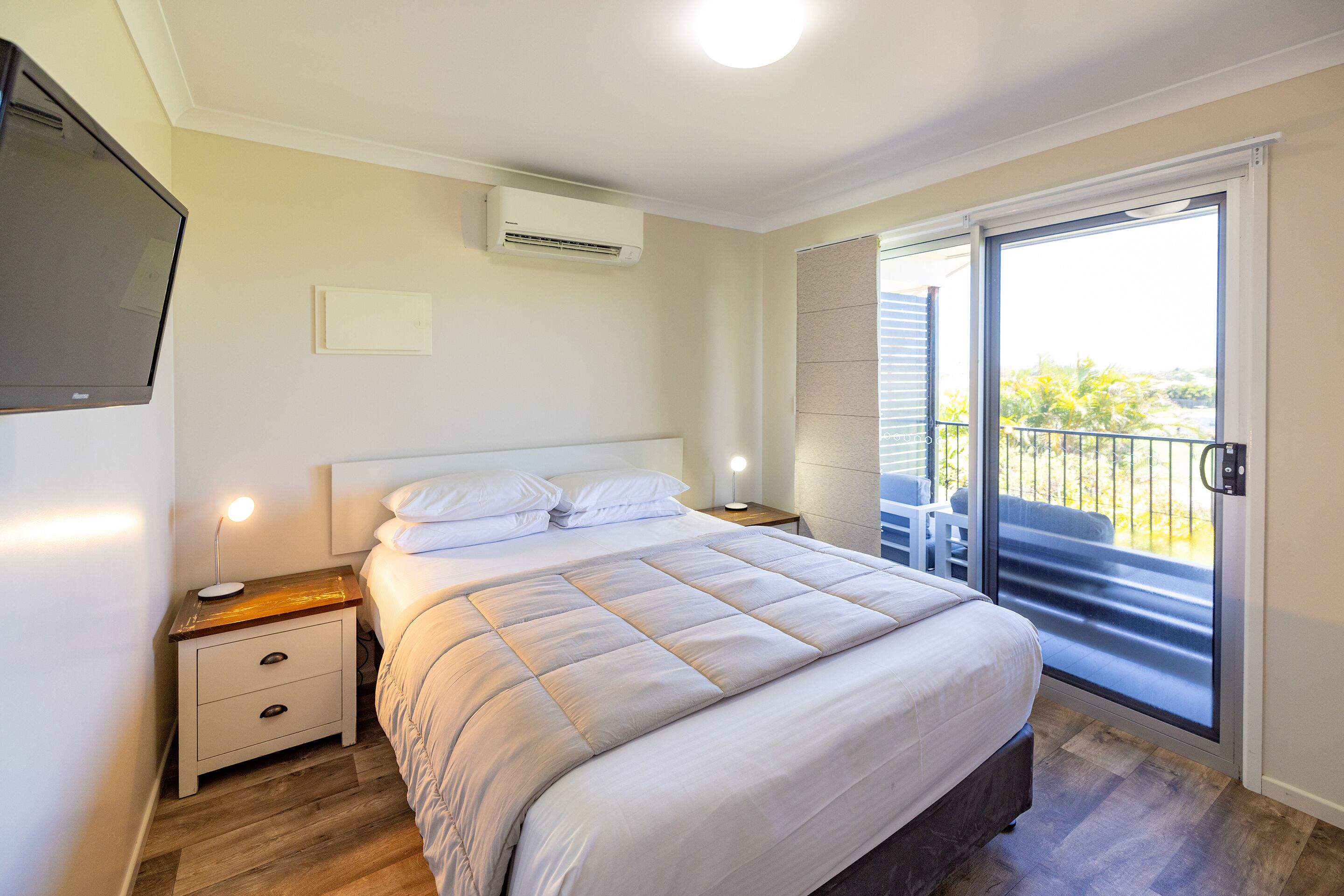 Ein Schlafzimmer mit Bett, Nachttischen, einer Klimaanlage und einer Schiebeglastür zum Balkon.