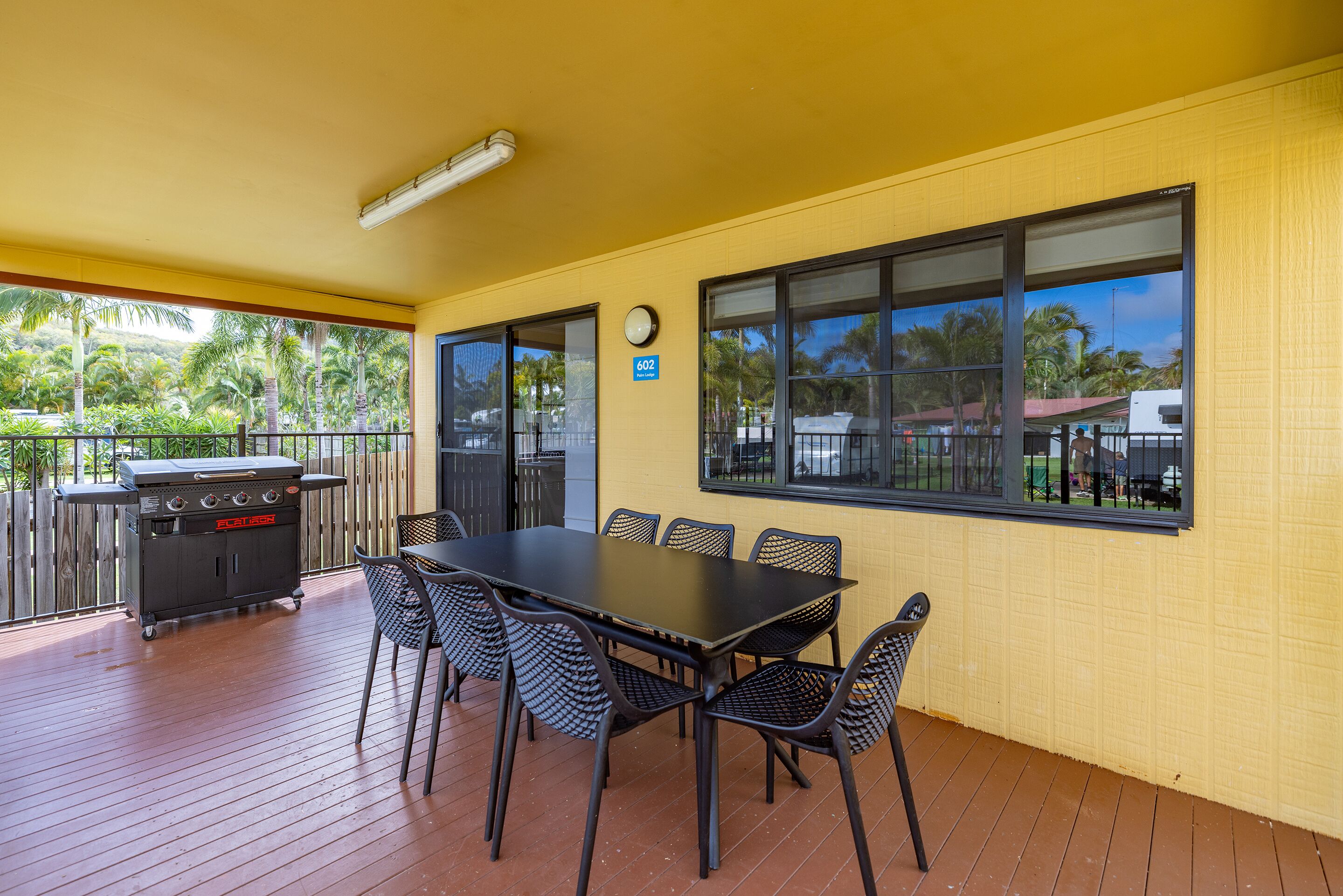 Une terrasse couverte avec une table et des chaises, un barbecue et une horloge au mur.