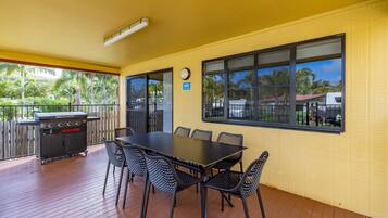 Une terrasse couverte avec une table et des chaises, un barbecue et une horloge au mur.