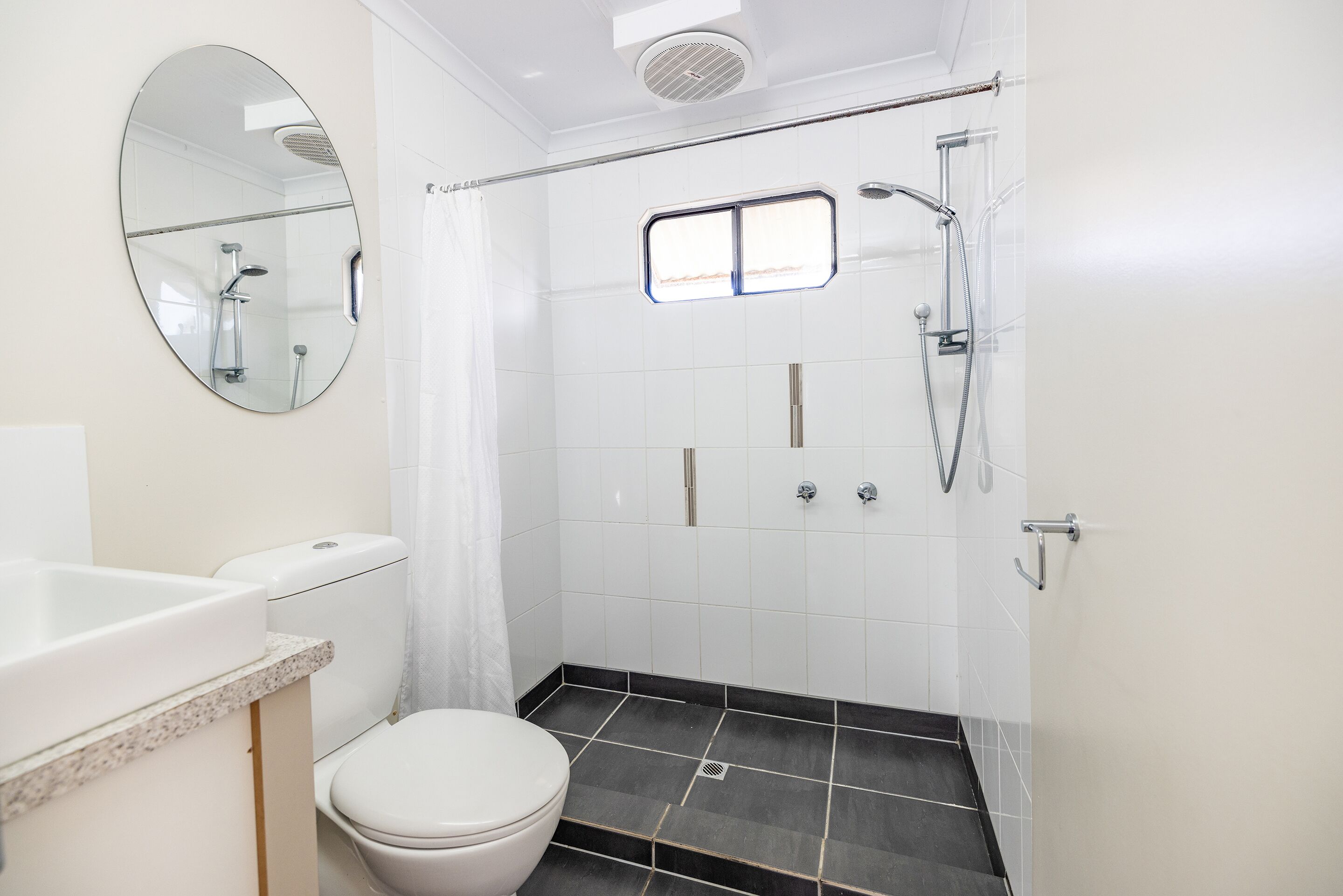 Een badkamer met toilet, wastafel, spiegel, douche en raam.