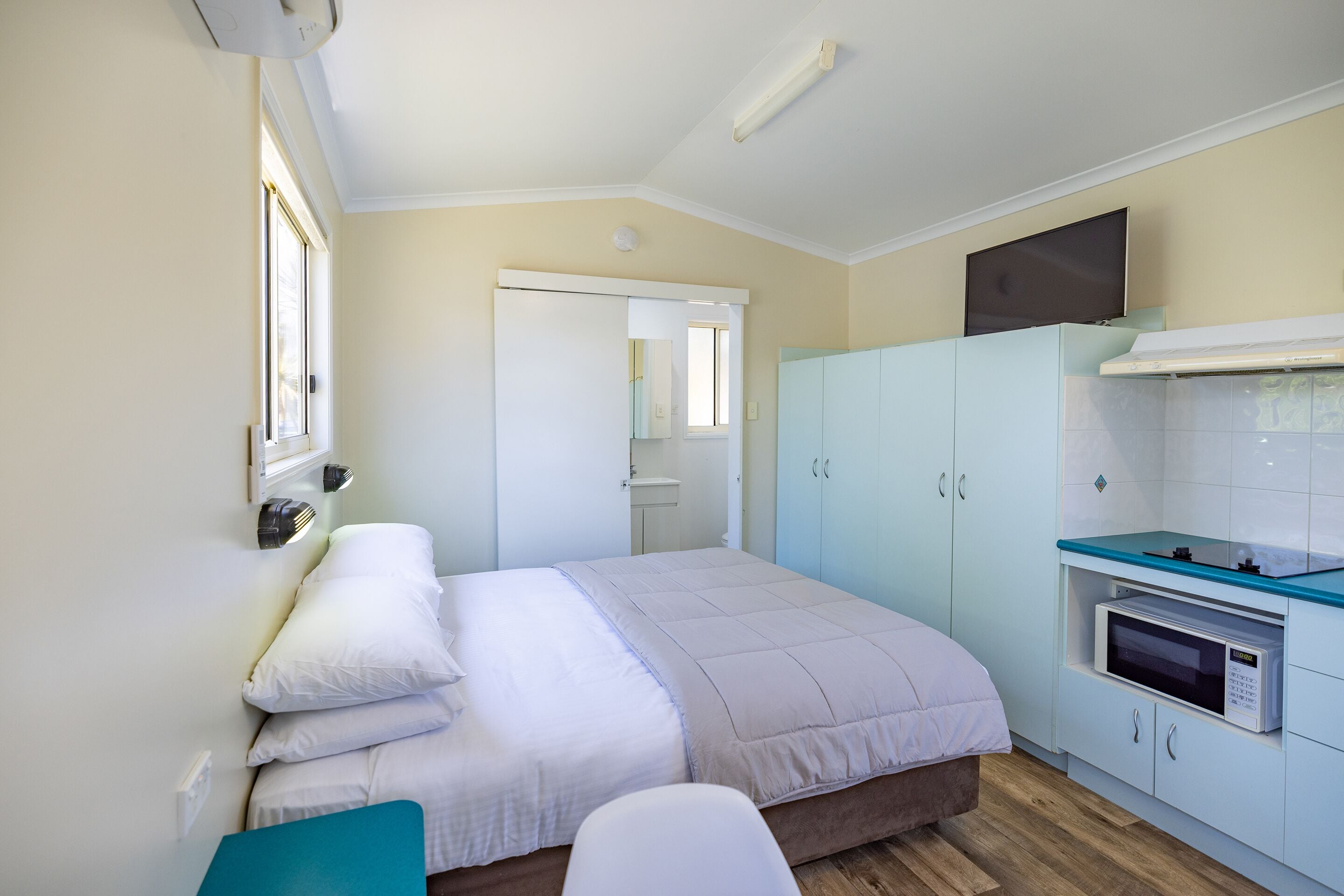 A bedroom with a bed, a bedside table, a wardrobe, and a kitchenette with a microwave.