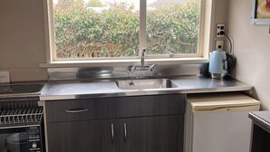 A compact kitchen with a built-in dishwasher, a sink, and a window overlooking a garden. - Aorangi Motel (Fairlie)