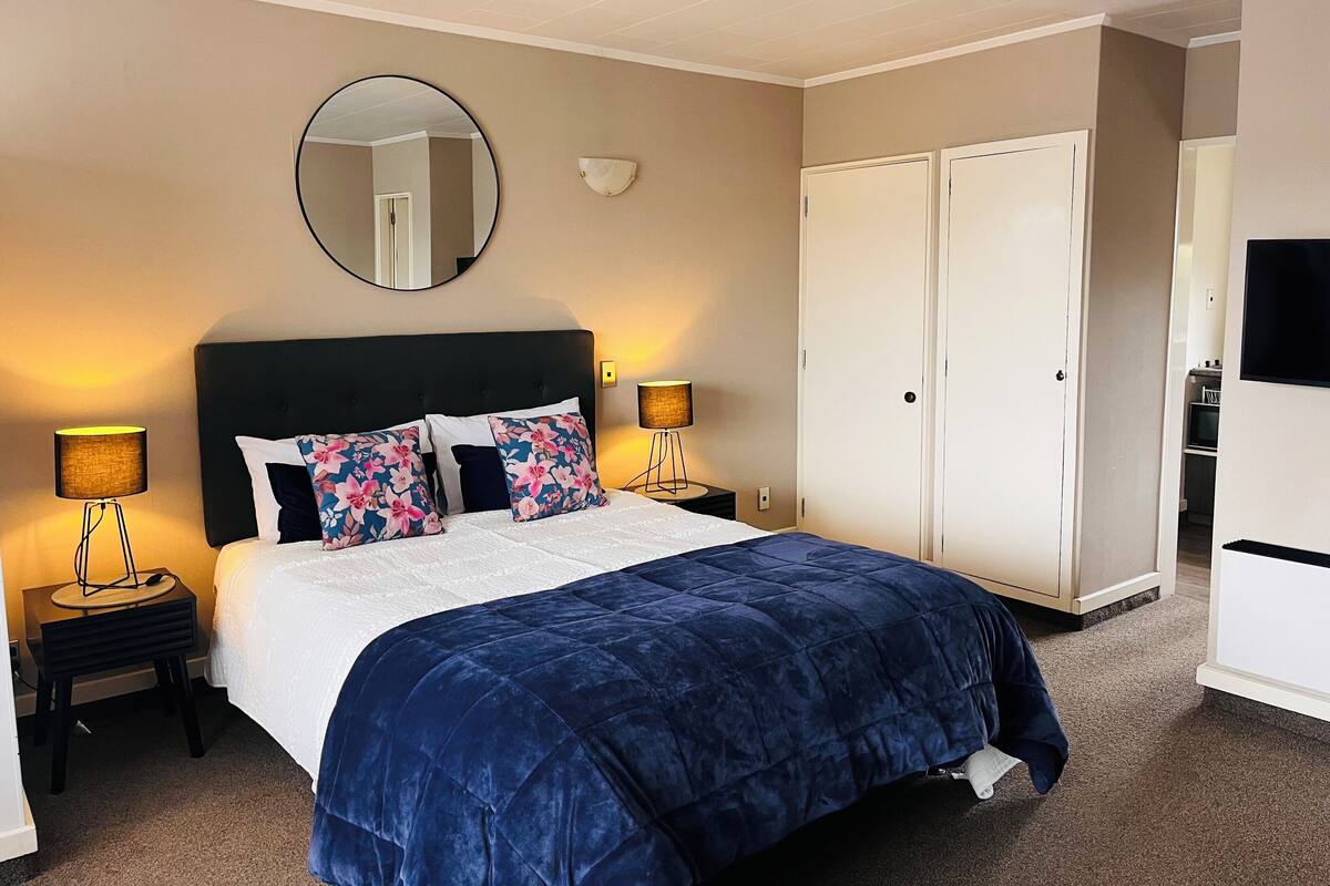 A hotel room with a large bed, two bedside lamps, a round mirror, and a wardrobe.