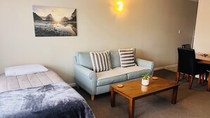 A room with two beds, a sofa, a coffee table, a desk, and a wall-mounted lamp. - Aorangi Motel (Fairlie)