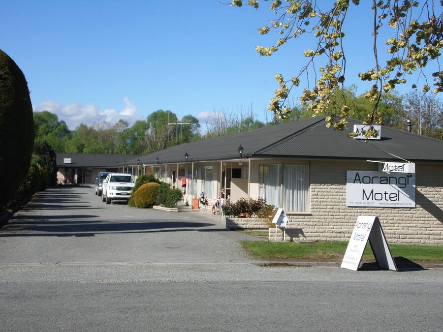 Un motel avec un panneau indicateur, un parking et un bâtiment doté d’un toit sombre.