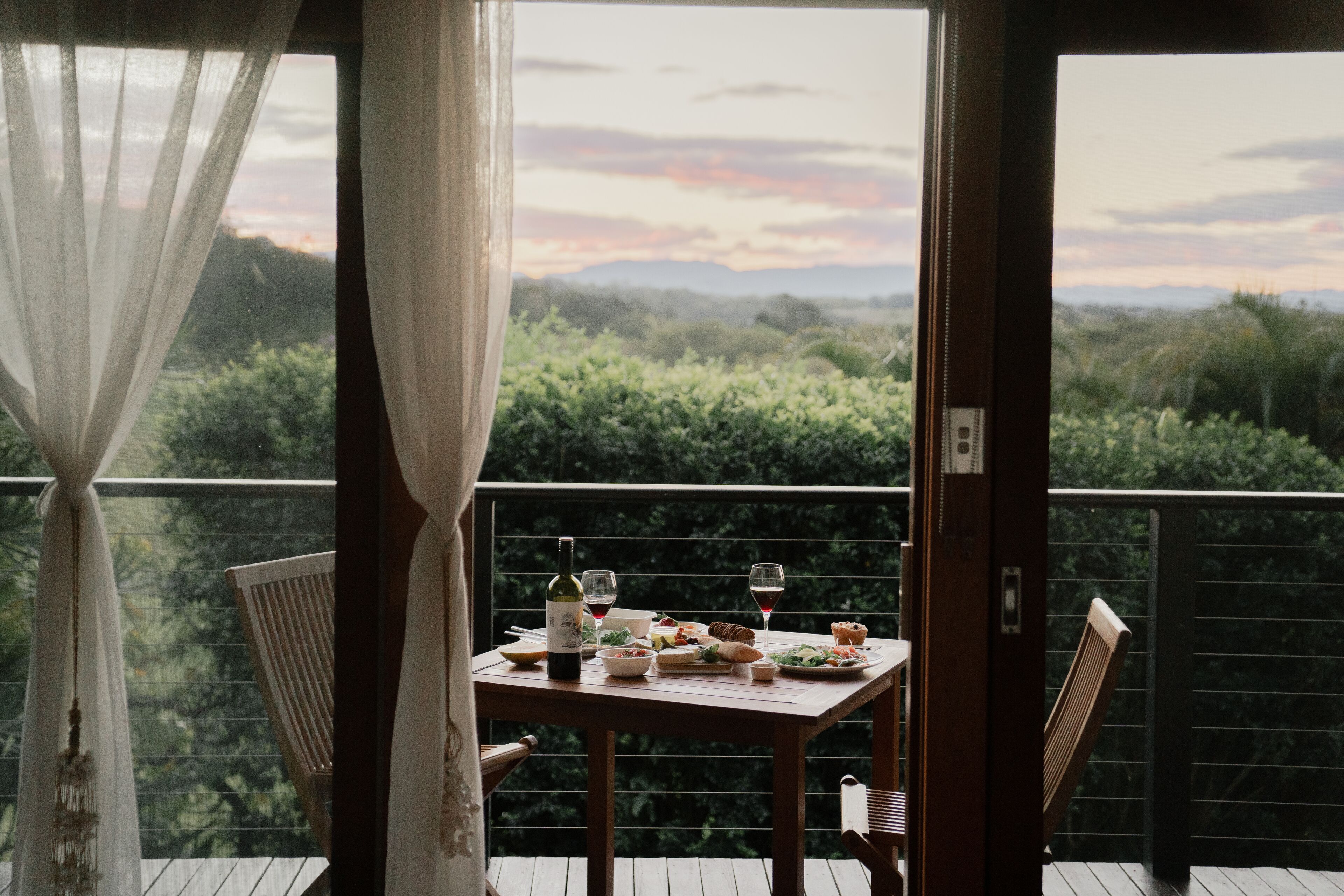A balcony with a table set for a meal, overlooking a lush landscape.