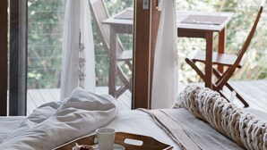 Une chambre avec un lit en bois, un plateau de petit-déjeuner et une vue sur la verdure à travers des rideaux transparents.