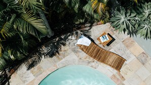 Un espace piscine avec un fauteuil de relaxation en bois et une petite table sur laquelle est posée une peinture.