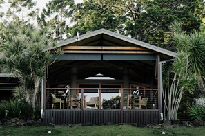 A covered outdoor seating area with chairs and tables, surrounded by lush greenery and trees. - Cape Byron Retreat (Skinners Shoot)