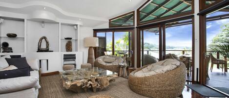 A spacious living area with a large glass window, a sofa, a wicker chair, and a coffee table.