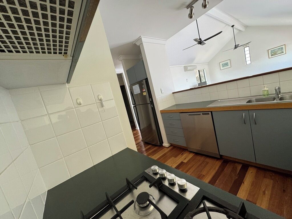 A modern kitchen with a gas stove, stainless steel appliances, and a wooden floor.