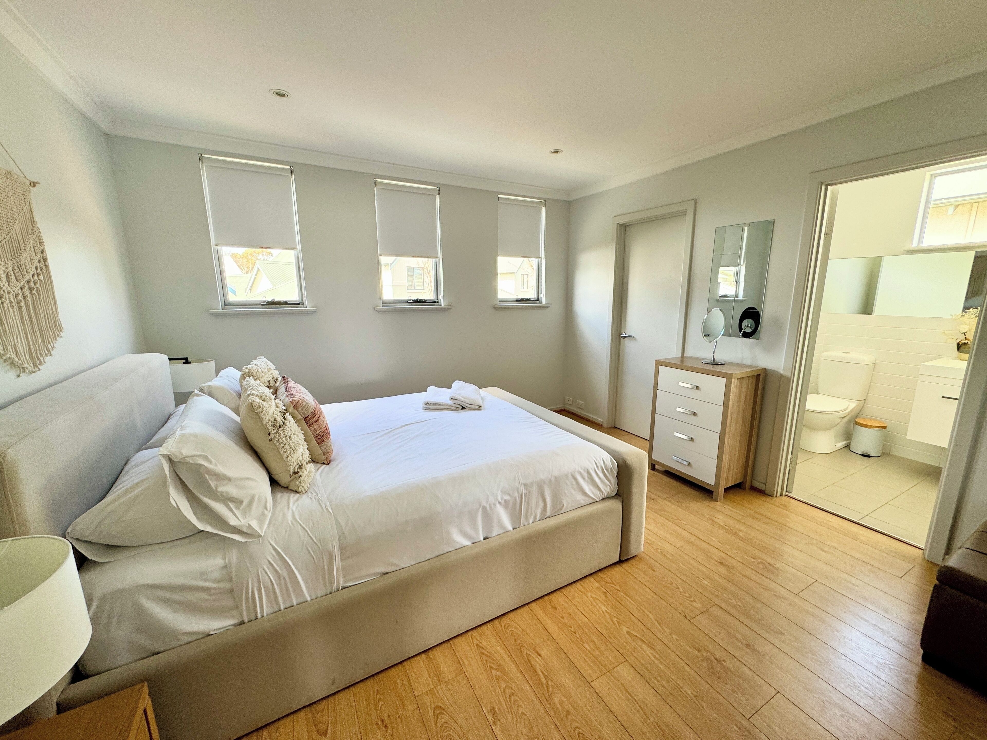 A bedroom with a large bed, a dresser, a mirror, and a view of the bathroom.