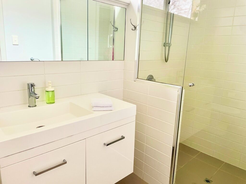 A bathroom with a white vanity, a mirror, a glass shower enclosure, and a green bottle of hand soap.