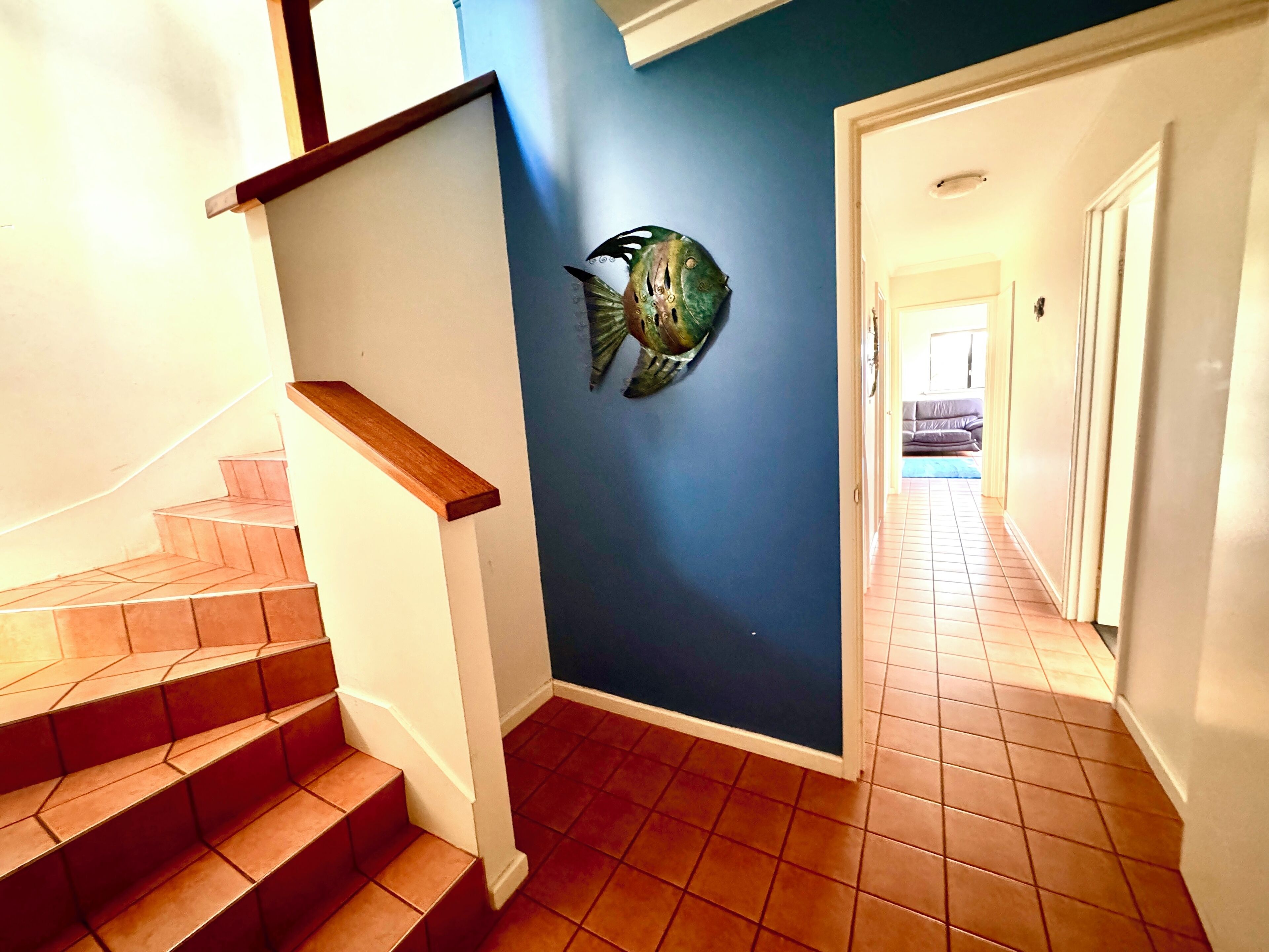 A staircase with wooden handrails leading to a room with a blue wall and a fish decoration.