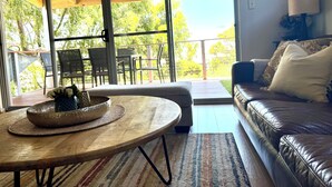 A living room with a sofa, a round wooden table with a woven basket, and a view of the outdoors through large windows. - The Break, Margaret River Beach Houses (Gnarabup)
