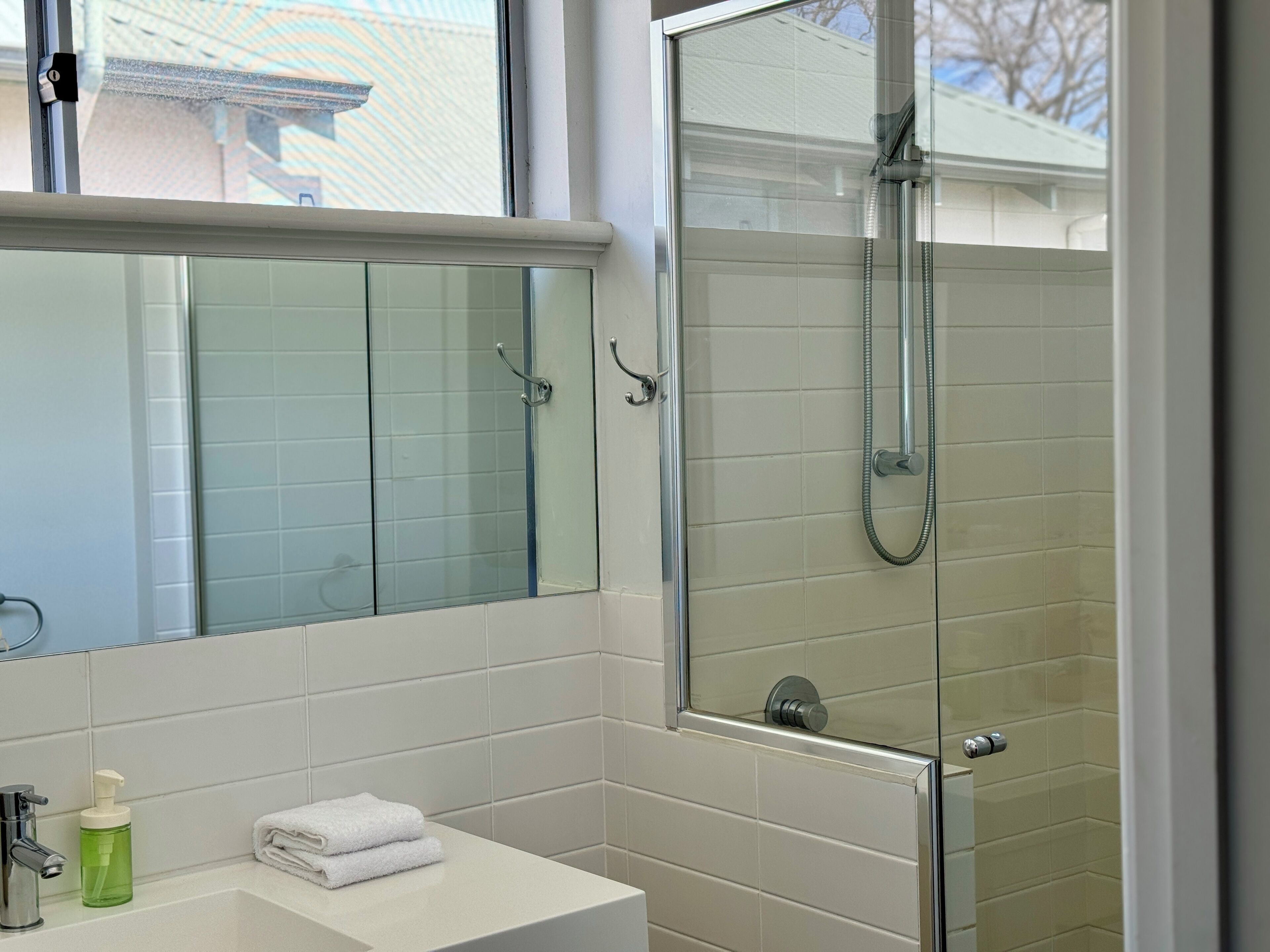 Une salle de bain avec une douche à parois de verre, un lavabo blanc doté d’un distributeur de savon et une serviette posée sur le comptoir.
