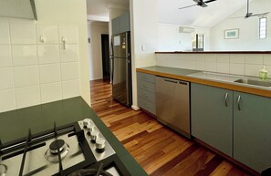 A kitchen with a gas stove, stainless steel refrigerator, wooden flooring, and grey cabinets.