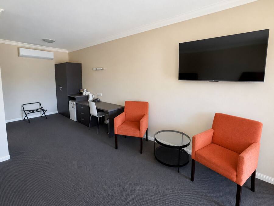 Et hotelværelse med et fladskærms-tv, to orange lænestole, et lille rundt bord, et skrivebord med stol, et minibar og et garderobeskab.