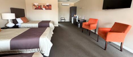 A hotel room with two beds, a desk, a chair, and a TV.