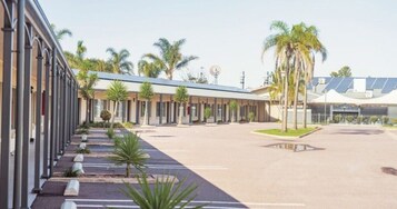 Un hotel con varias habitaciones, estacionamiento y palmeras.