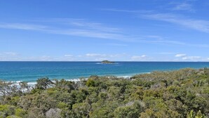 A coastal landscape with dense greenery in the foreground and a clear view of the ocean and a small island in the distance. - Marcoola Beach Resort (Marcoola)