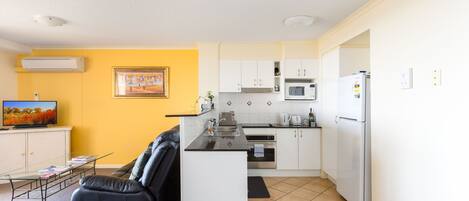 A compact living space with a kitchenette, a sofa, a coffee table, and a television.
