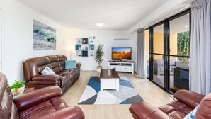A modern living room with leather sofas, a flat-screen TV, and a large window with a view of the outdoors. - Marcoola Beach Resort (Marcoola)