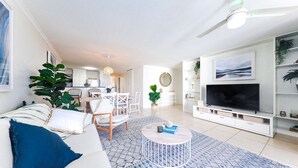 A modern living room with a sofa, coffee table, TV, and dining area. - Marcoola Beach Resort (Marcoola)