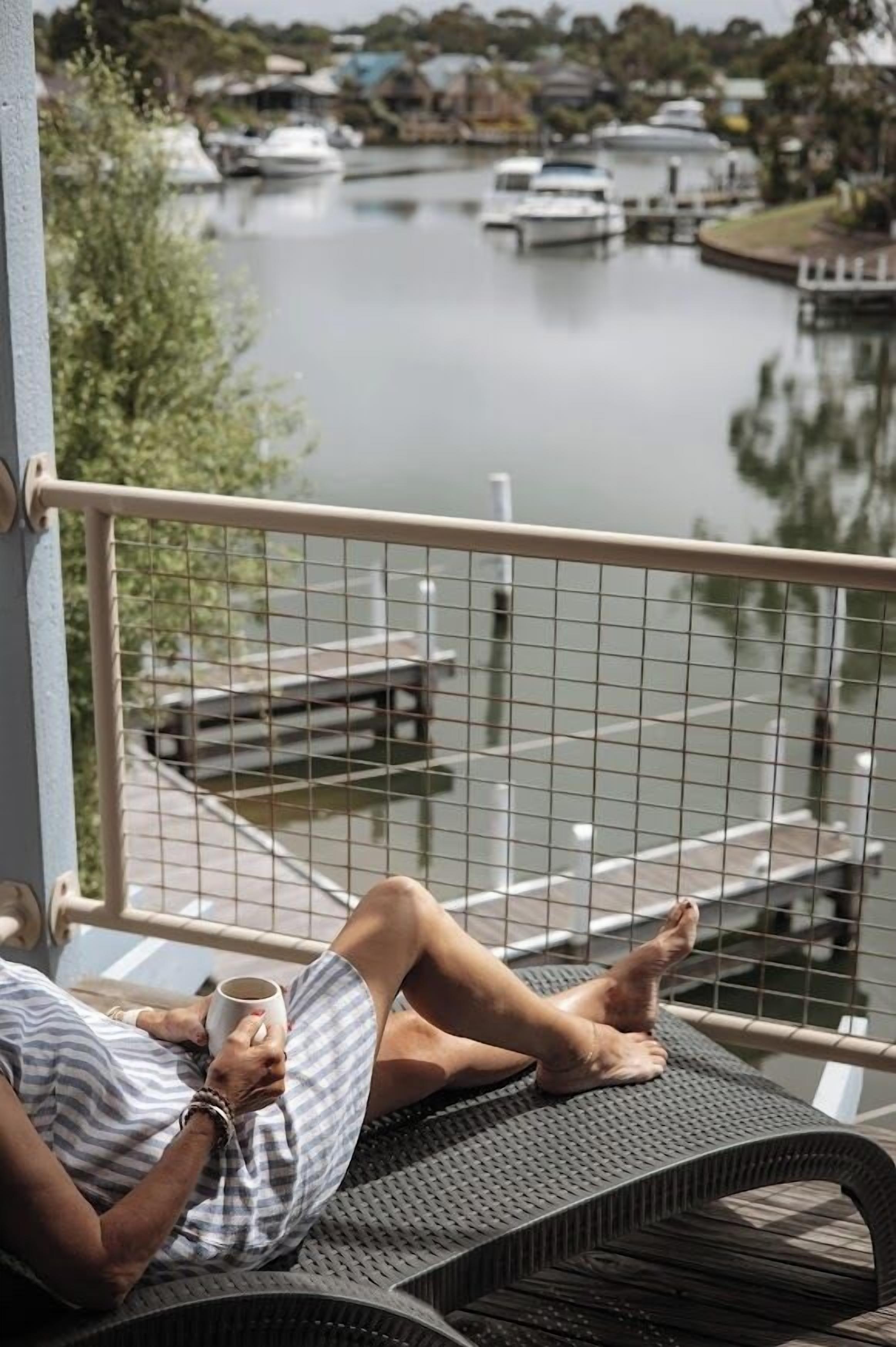 Iemand ontspant op een balkon met uitzicht op een kalm meer en aangemeerde boten.
