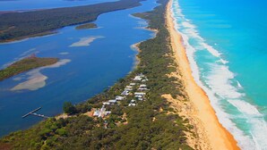An aerial view of a coastal area with a long stretch of beach, clear blue waters, and a row of buildings along the shore. - Captains Cove Waterfront Resort (Paynesville)
