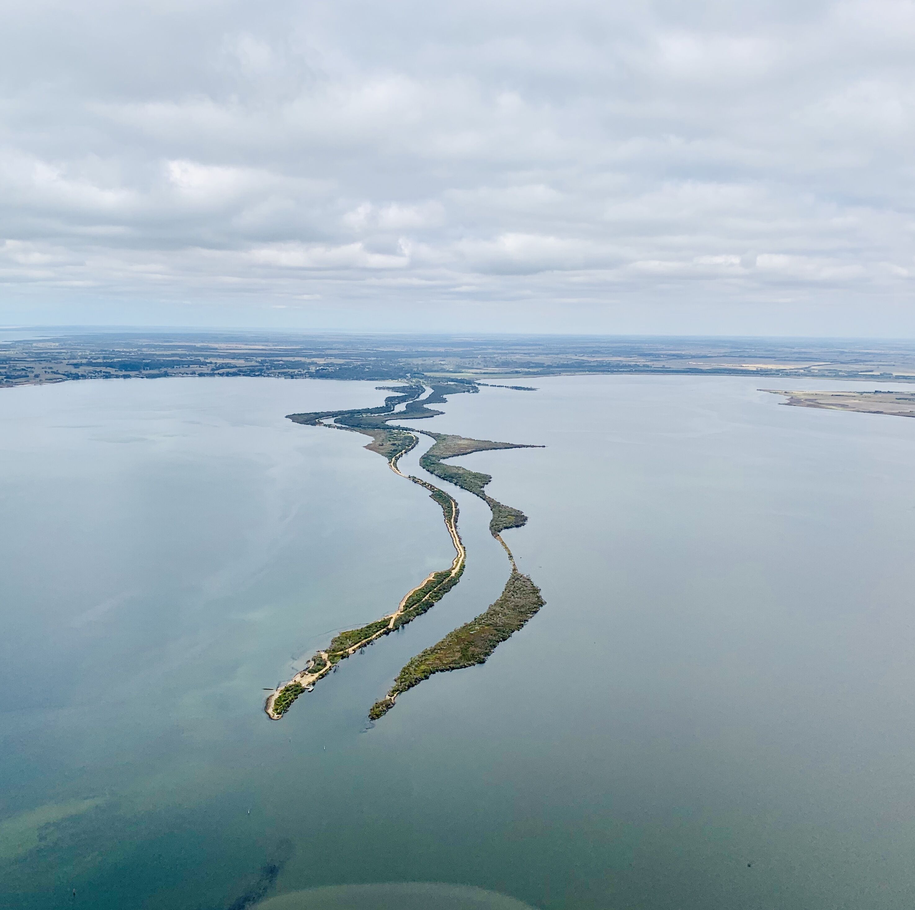 An aerial view of a coastal area with a series of connected islands and a long, narrow peninsula.
