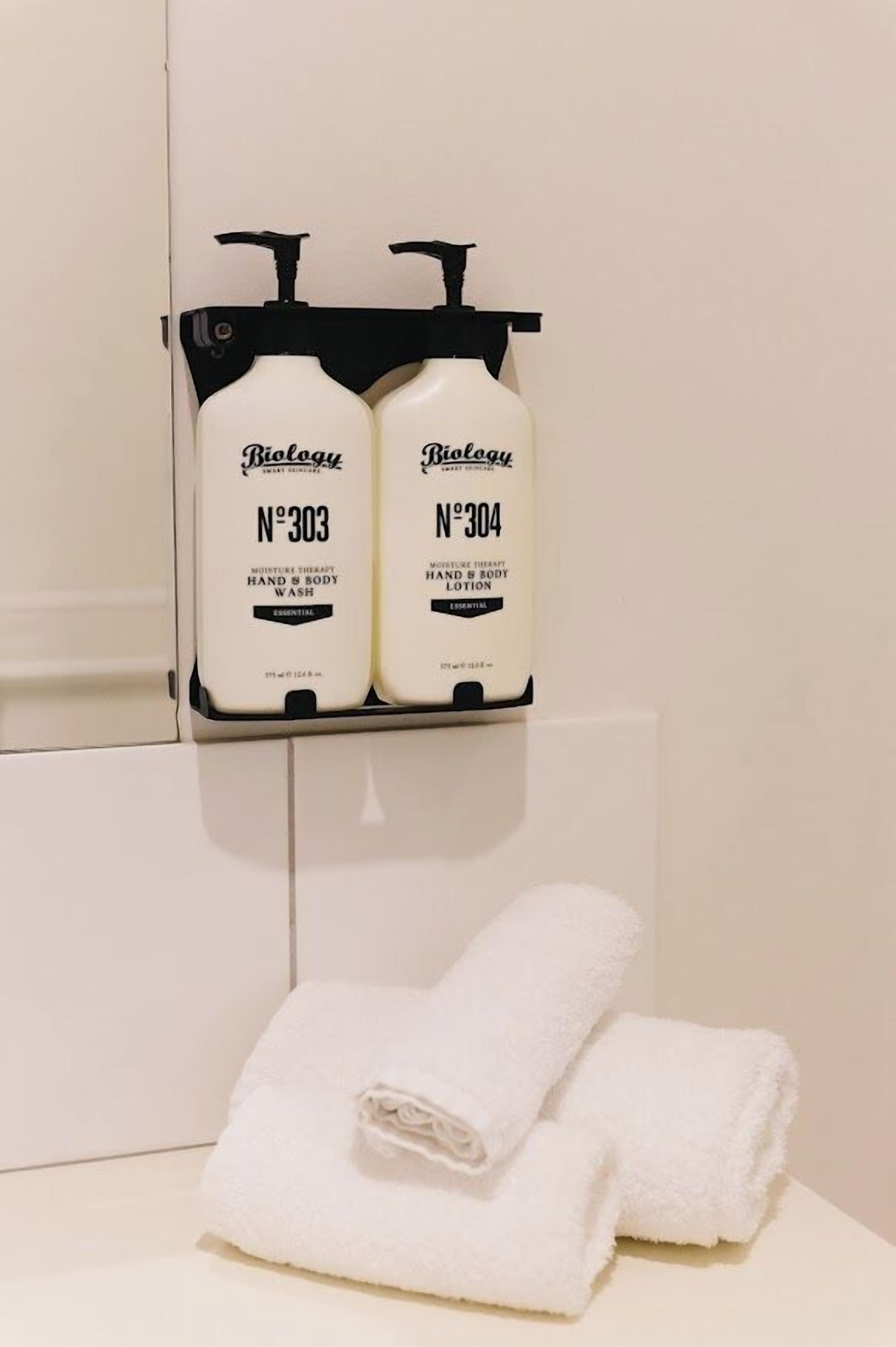 Dos botellas de jabón de manos y cuerpo en un dispensador negro en un baño.