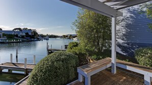 A wooden deck with a view of a calm river and dock, surrounded by greenery and a white building. - Captains Cove Waterfront Resort (Paynesville)