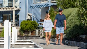 A couple walking on a wooden boardwalk with a blue building in the background. - Captains Cove Waterfront Resort (Paynesville)